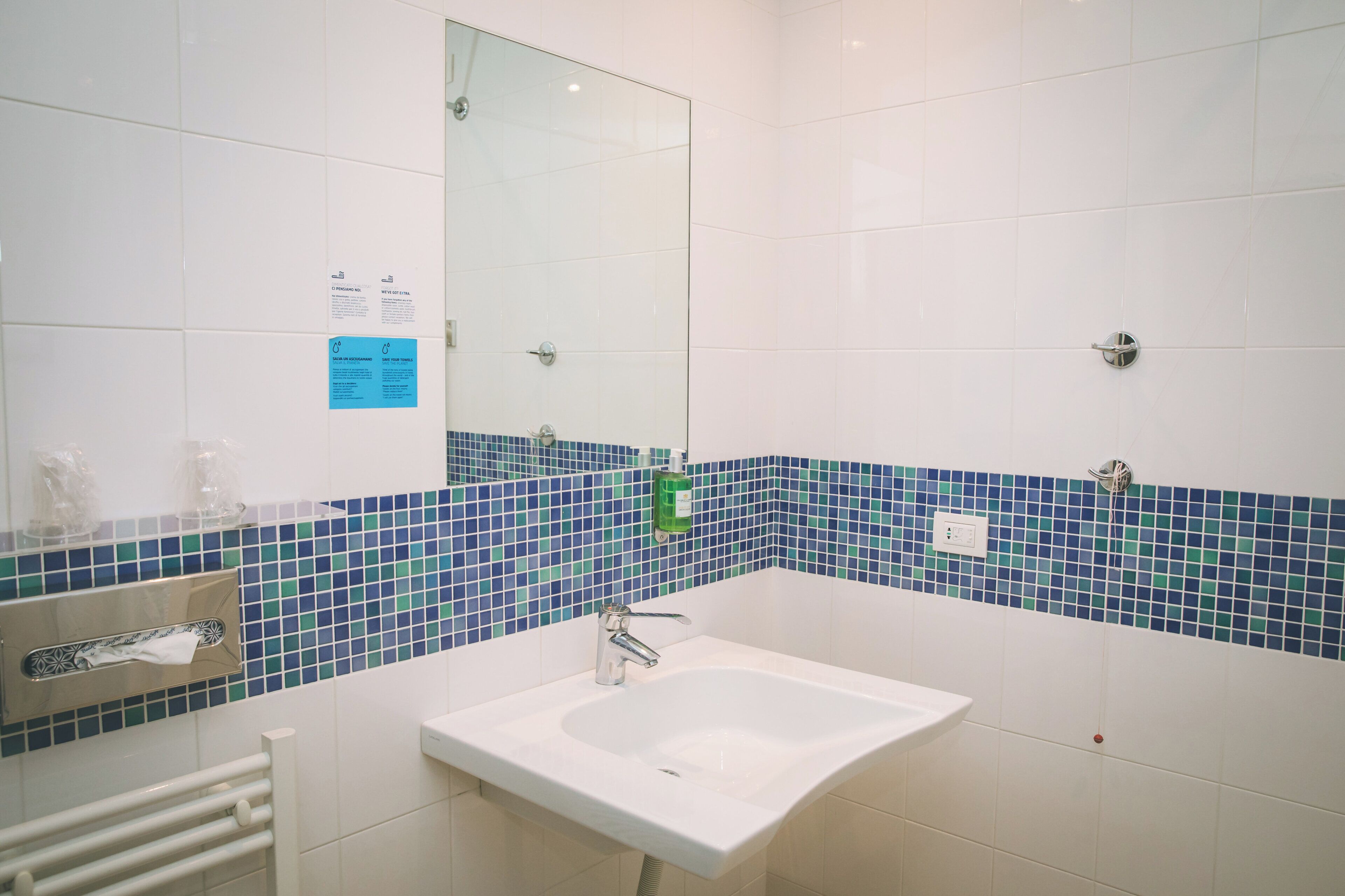 A bathroom with a white sink, a mirror, and a blue-tiled wall.