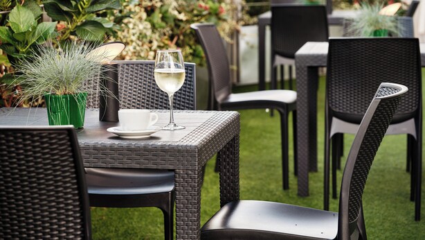 An outdoor patio with wicker tables and chairs, a glass of white wine, and a potted plant. - Holiday Inn Express Milan - Malpensa Airport by IHG (Somma Lombardo)
