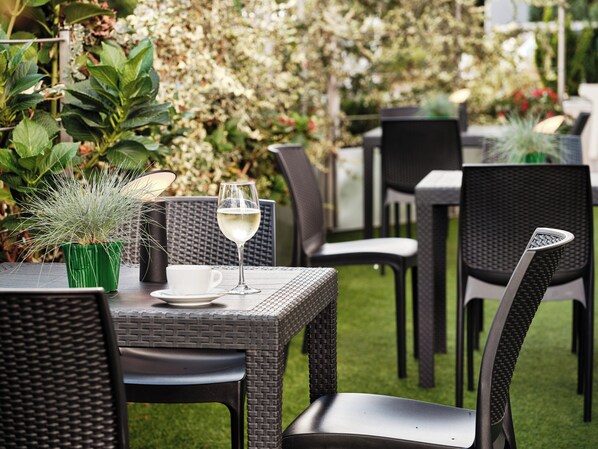 Eine Terrasse im Freien mit Korbmöbeln, einem Glas Weißwein und einem Blumentopf.
