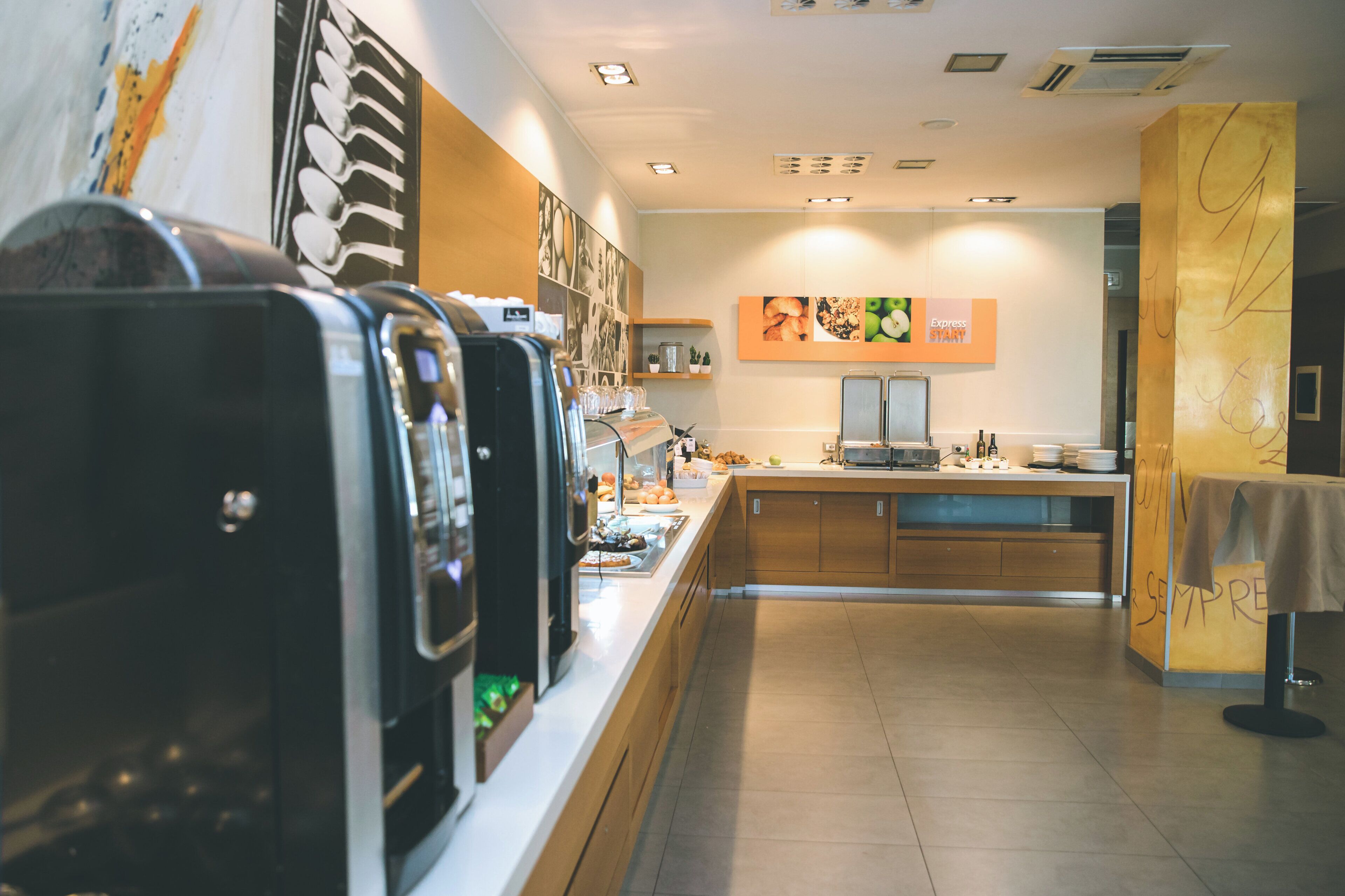 L’intérieur d’un café, avec des machines à expresso, un comptoir où sont exposées des pâtisseries et un mur servant de présentoir pour les aliments.