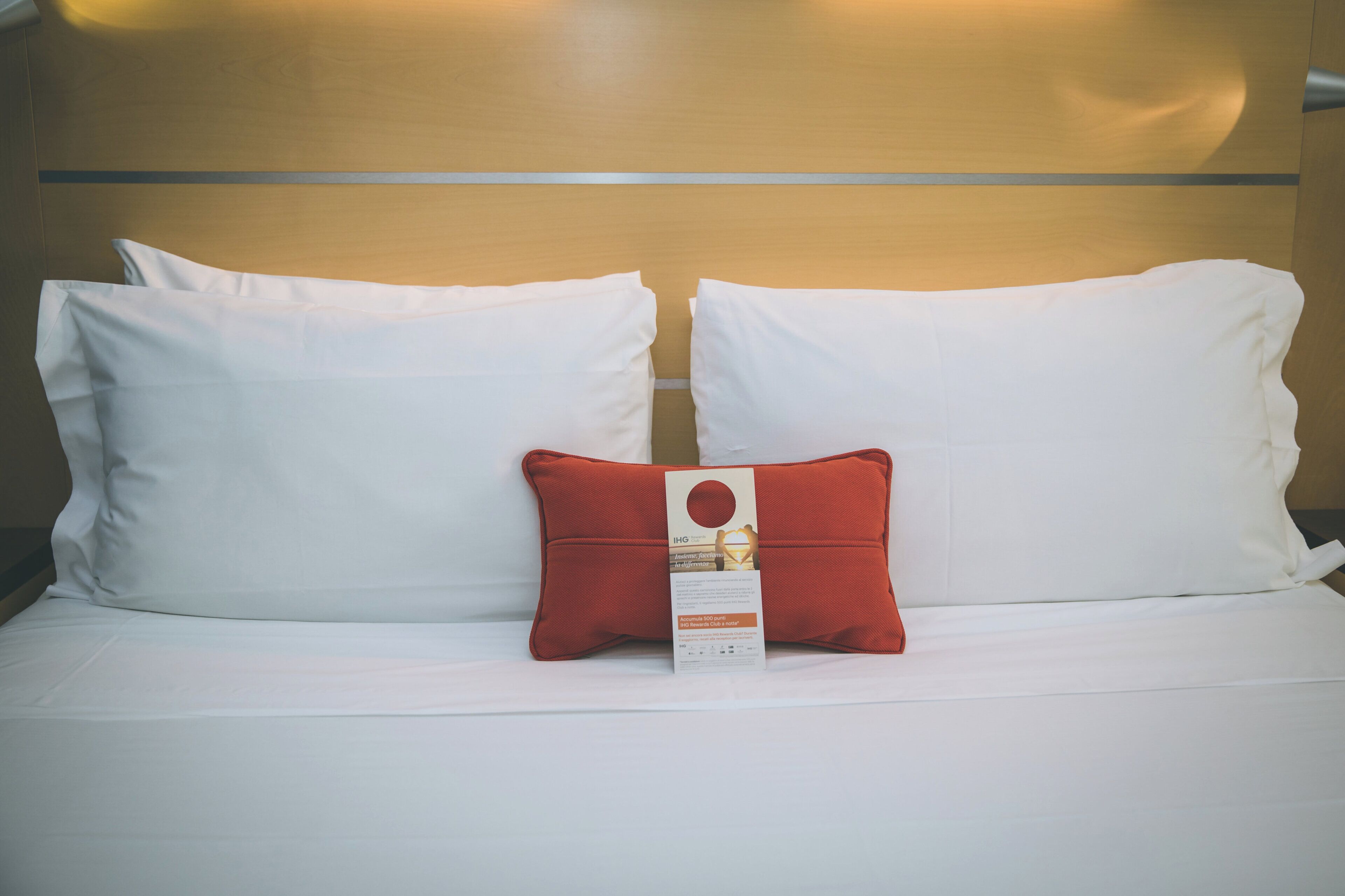 Une chambre d’hôtel avec un lit agrémenté de deux oreillers blancs et d’un oreiller décoratif rouge.