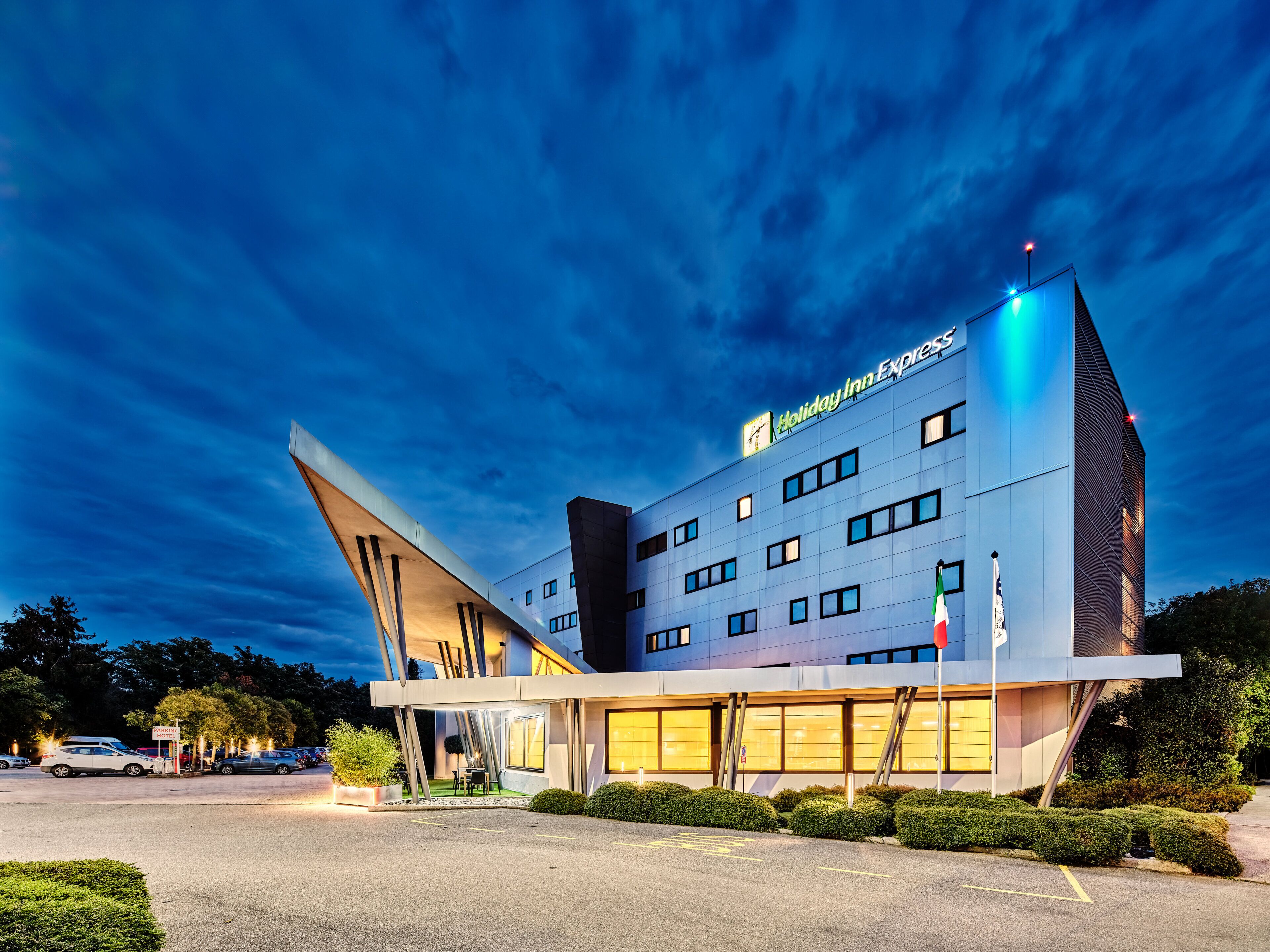 Um moderno hotel Holiday Inn Express com um design arquitetônico único, destacando uma marquise saliente e um estacionamento.