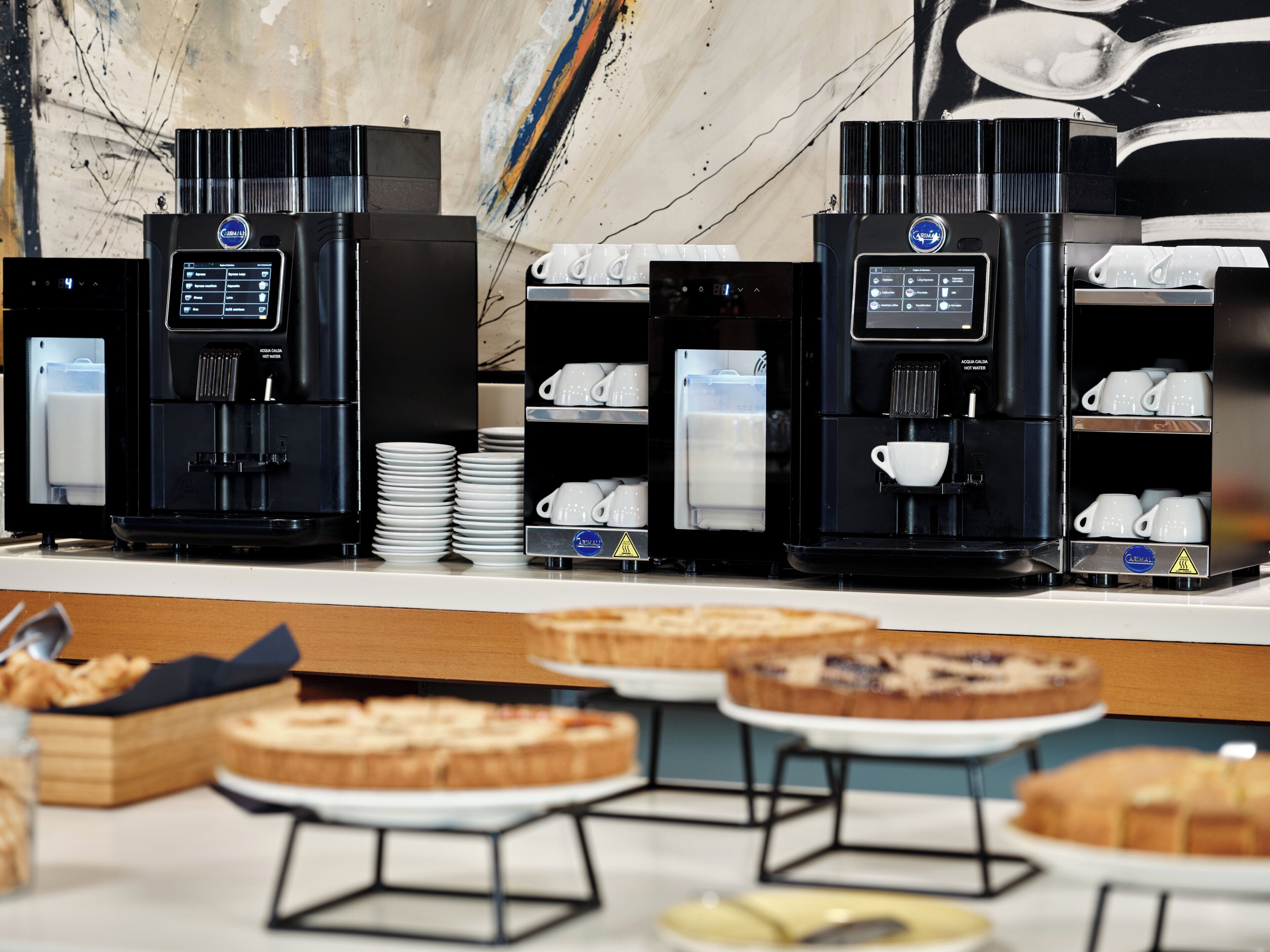 A coffee station with multiple espresso machines and a variety of coffee cups and saucers.