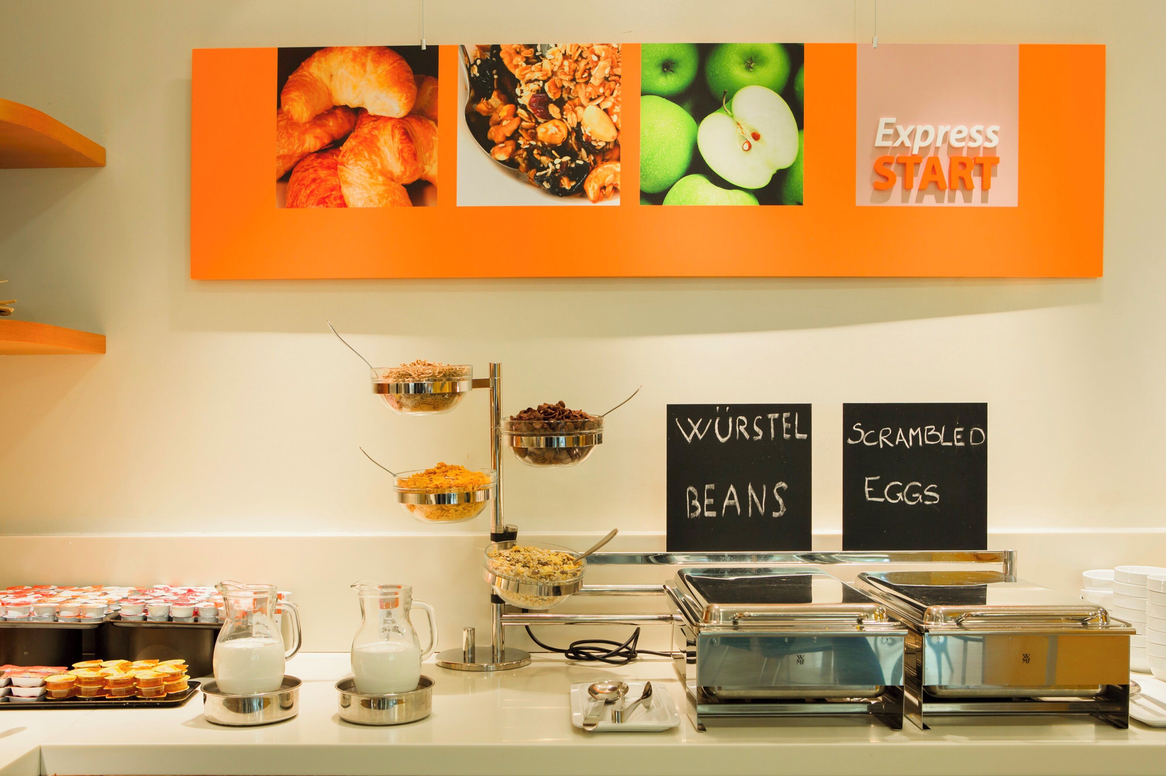 Zona de bufé con opciones de comida señalizadas, incluyendo frijoles y huevos revueltos.