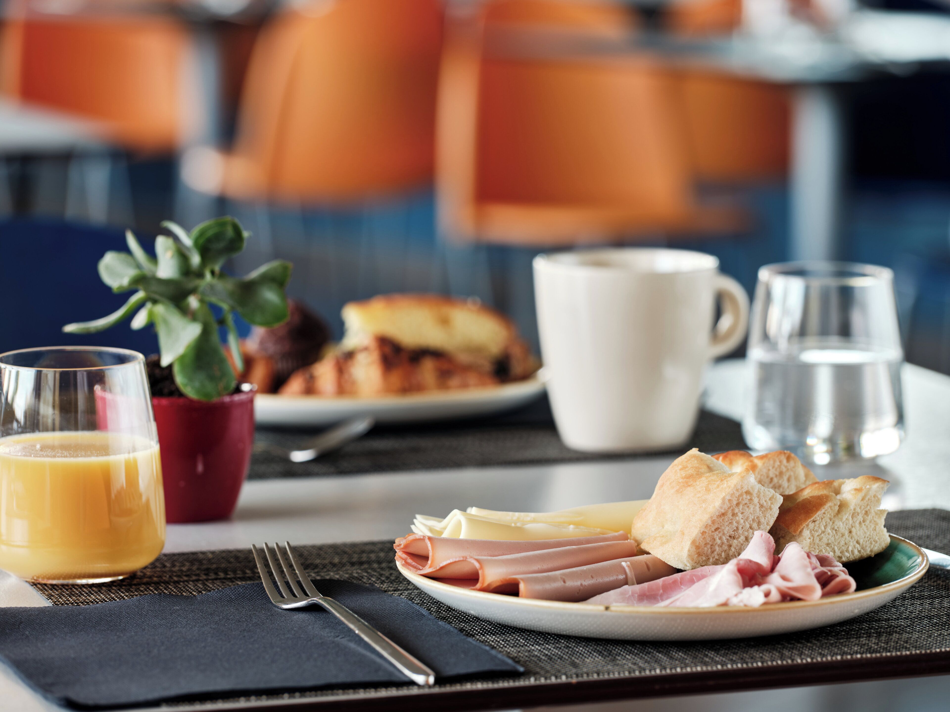 A breakfast setting with a plate of ham and cheese, a glass of orange juice, a cup of coffee, and a glass of water.