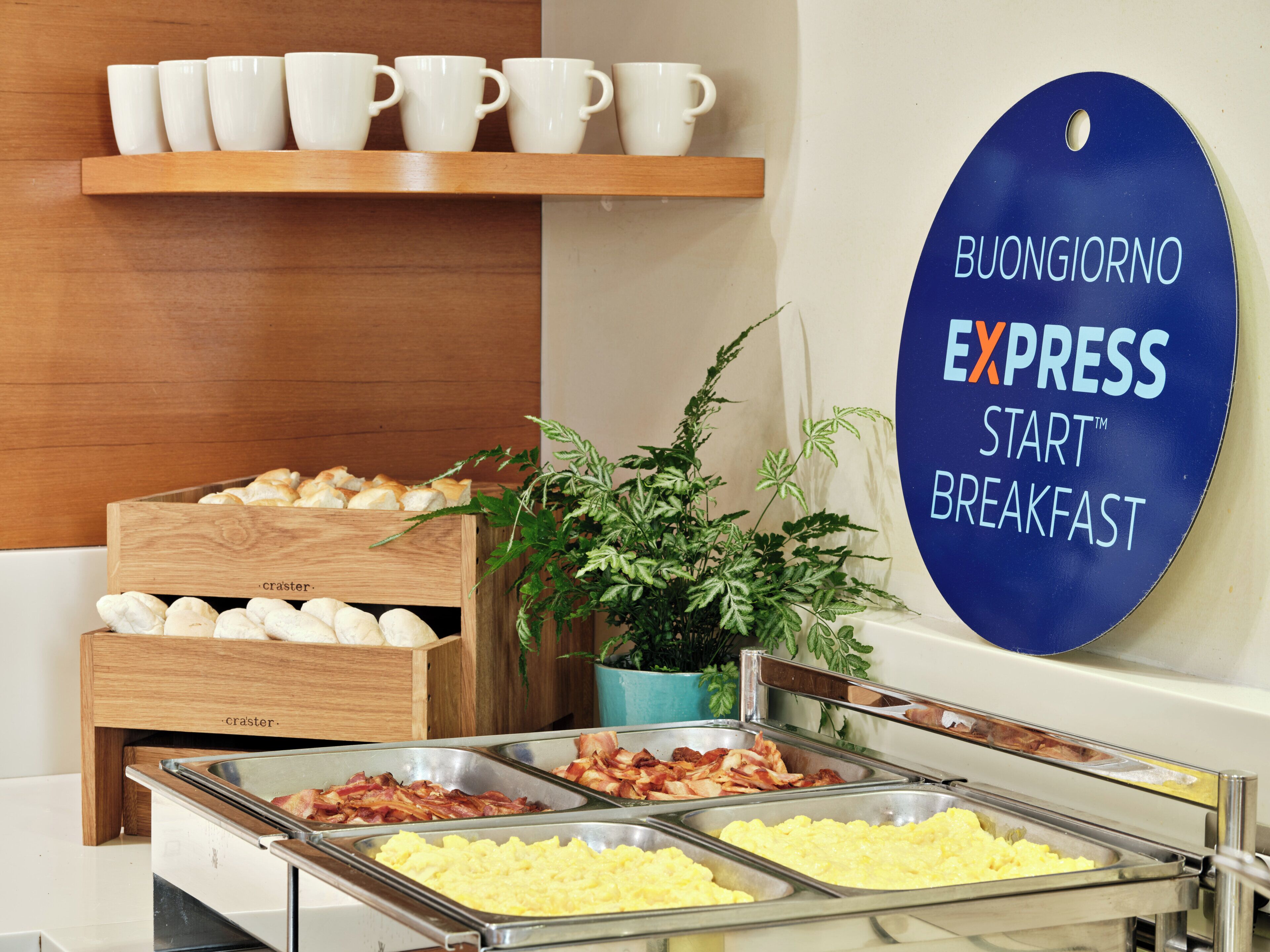 A buffet breakfast area with various food options, a sign for 'BUONGIORNO EXPRESS START BREAKFAST', and a plant in the corner.