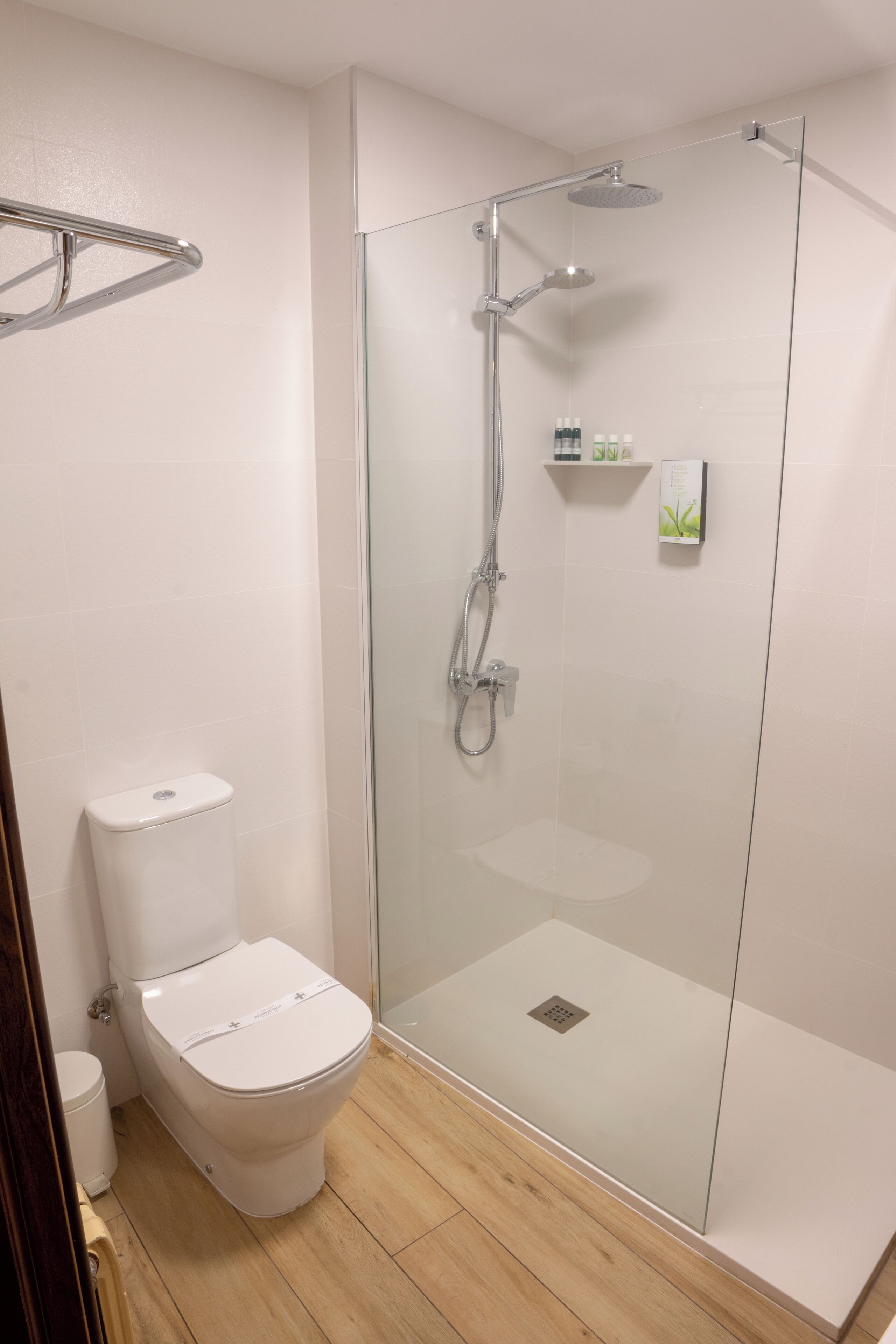 A modern bathroom with a glass-enclosed shower, a white toilet, and a wooden floor.