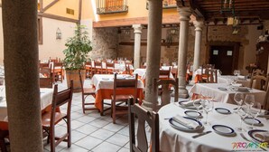 An indoor dining area with tables set for multiple guests, wooden chairs, and a potted plant. - Hotel Las Cancelas (Ávila)