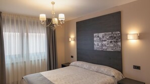 A modern bedroom with a large bed, a chandelier, a wall-mounted picture, and bedside lamps. - Hotel Las Cancelas (Ávila)