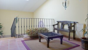 A balcony with a metal railing, a wooden bench, a small table, and a potted plant. - Hotel Las Cancelas (Ávila)