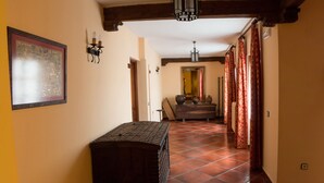 A hallway with a tiled floor, a wooden bench, a framed artwork on the wall, a door at the end, and a fire extinguisher on the right. - Hotel Las Cancelas (Ávila)