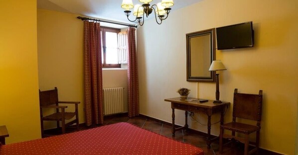 Una habitación de hotel con una cama, dos sillas, una mesa con lámpara, televisión y ventana con cortinas.