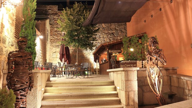 A restaurant entrance with stone steps, outdoor seating, and two metal sculptures. - Hotel Las Cancelas (Ávila)