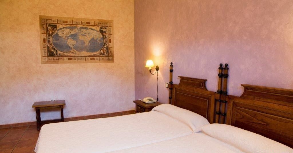 Un dormitorio con una cama grande, cabecera de madera, mesita de noche con lámpara y un mapa del mundo en la pared.