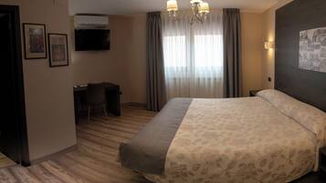Habitación de hotel con una cama grande, un escritorio, una silla, un televisor montado en la pared y un candelabro.