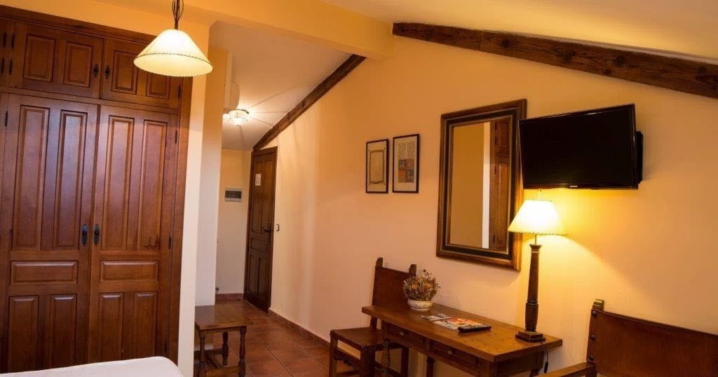 A hotel room with wooden furniture, a television mounted on the wall, and a lamp on a side table.