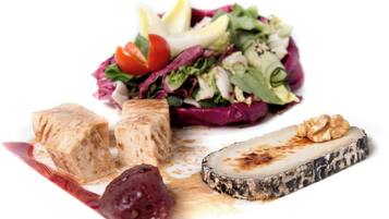 A plate with a variety of food items including tofu, a slice of cheese, a walnut, and a salad with mixed greens and cherry tomatoes.
