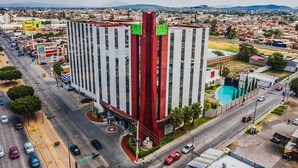 Un edificio de gran altura con una fachada prominente de rojo y blanco, varios balcones y una piscina en el patio.