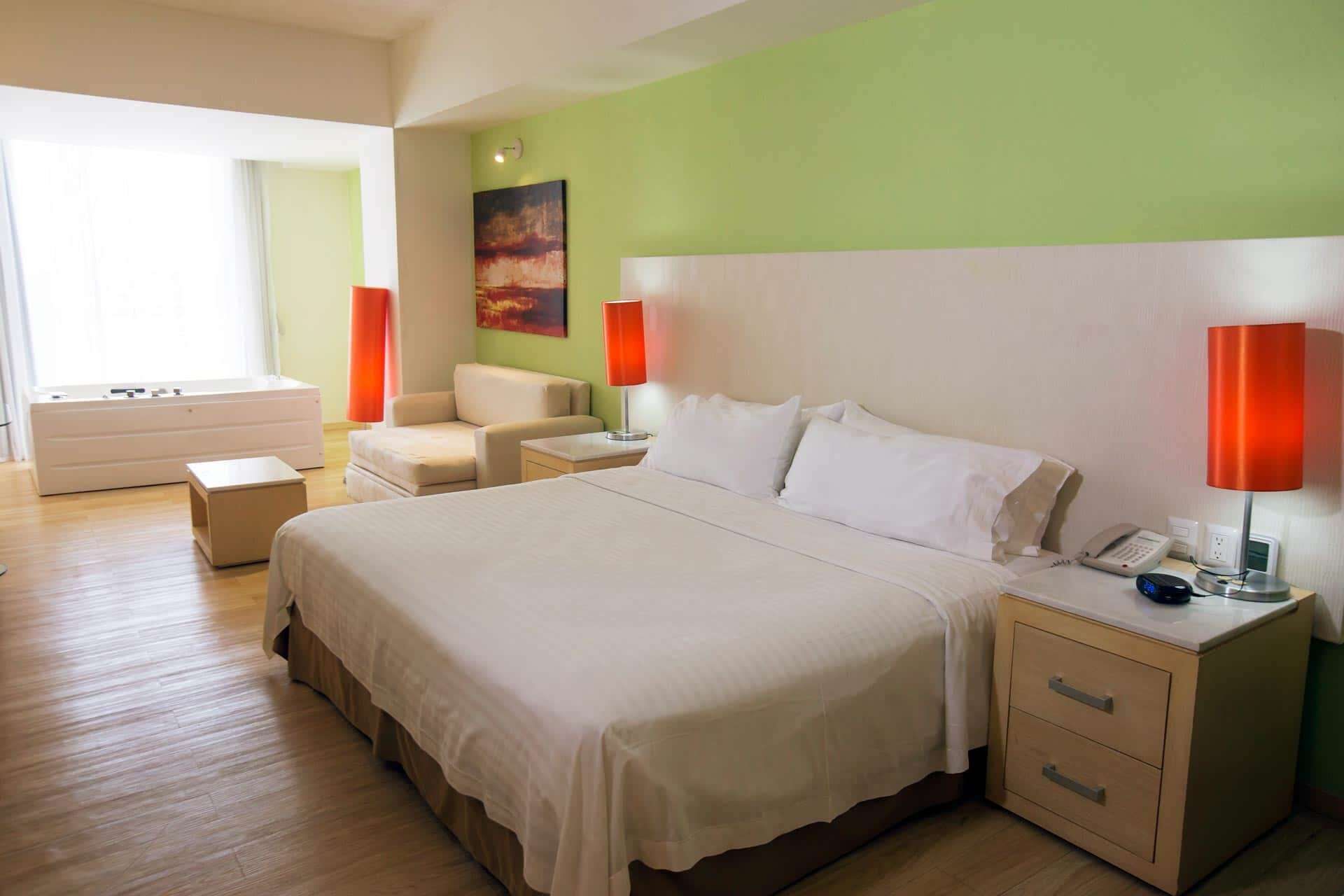 Ein Hotelzimmer mit einem großen Bett, einem Nachttisch mit Telefon, einem Sessel, einem kleinen Tisch und einem Fenster mit Vorhängen.