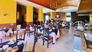 Un restaurante con varias mesas y sillas, una pantalla de televisión y una zona de cocina.
