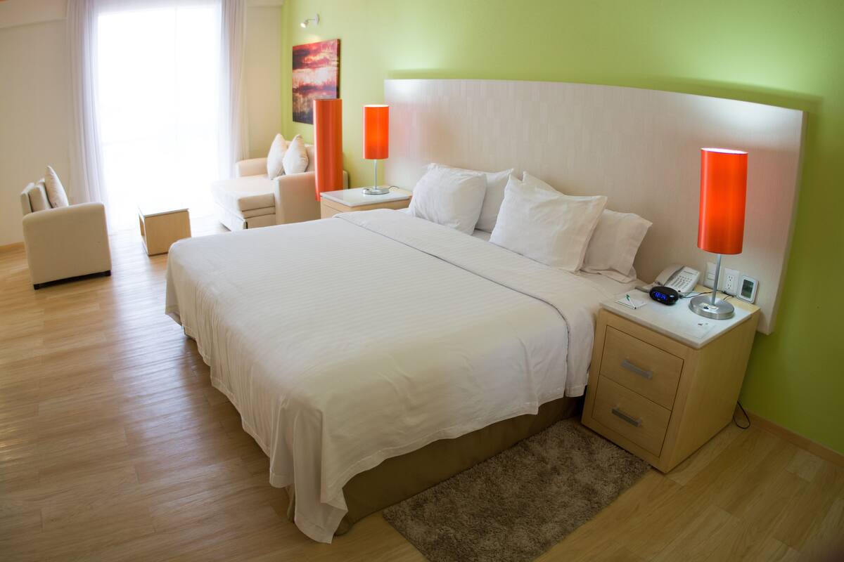 A hotel room with a large bed, bedside tables, a chair, and a nightstand with a lamp.