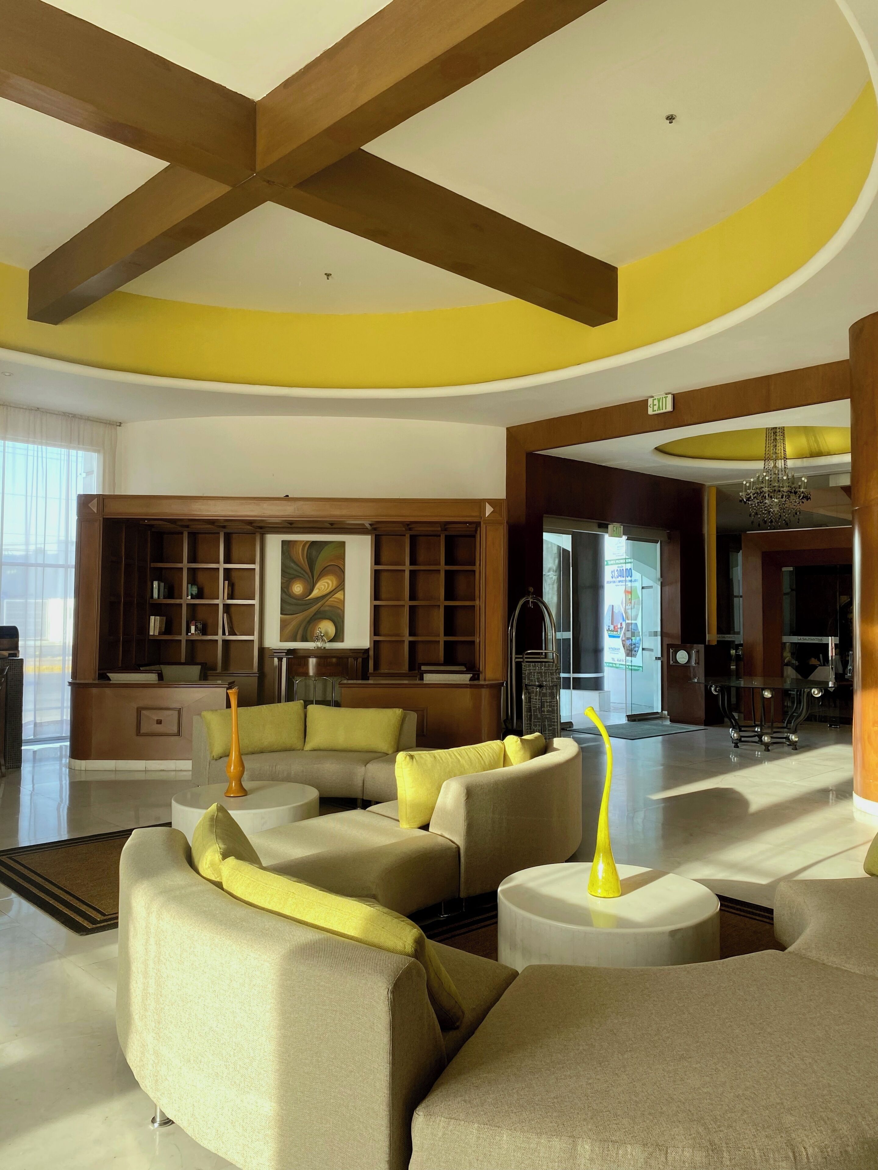 A spacious lobby with a high ceiling, wooden beams, a reception desk, and a large painting on the wall.