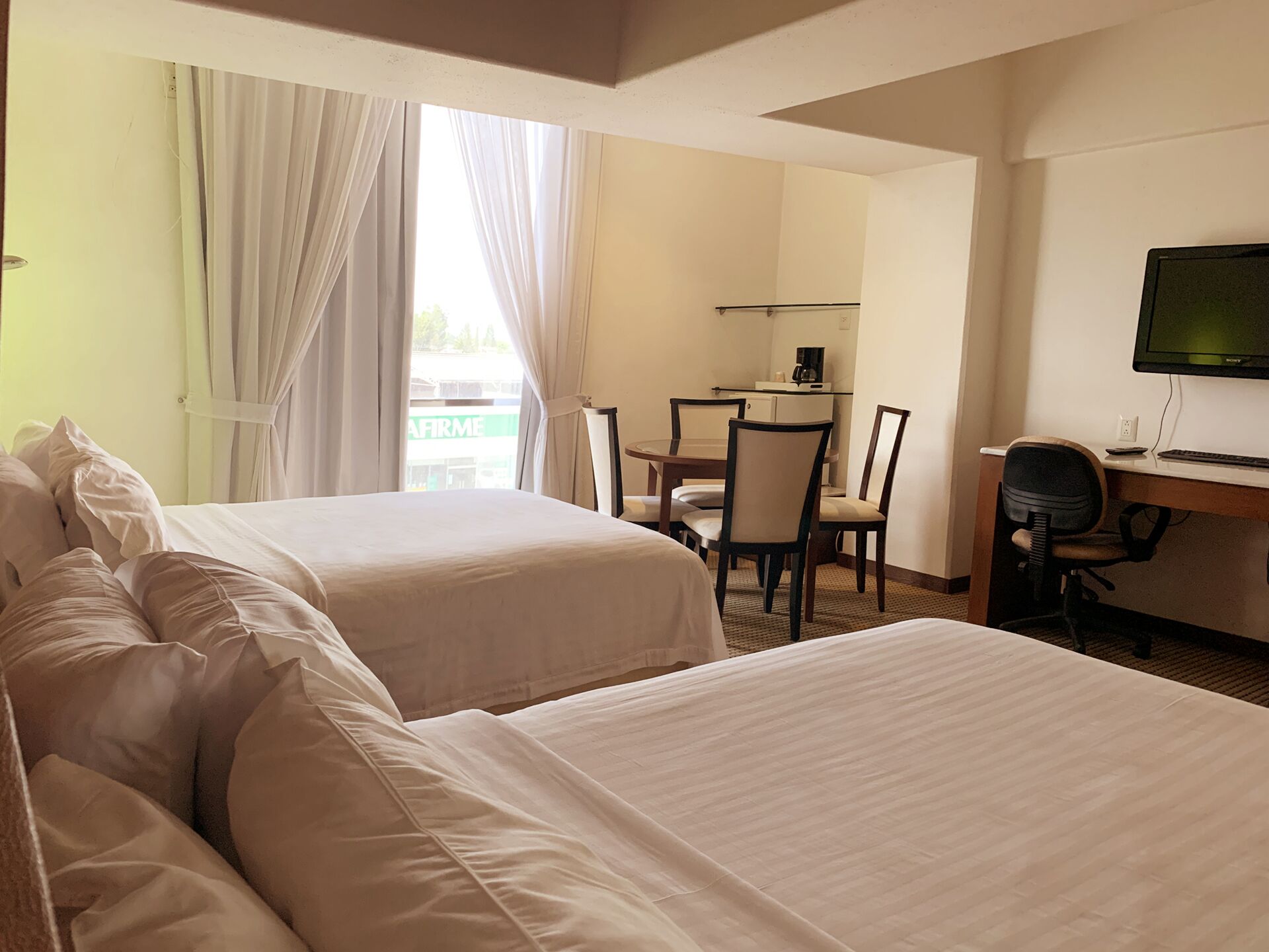 A hotel room with two beds, a desk with a chair, a television, and a window with curtains.