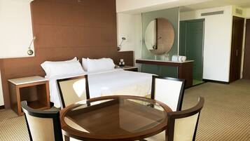 Habitación de hotel con cama, mesitas de noche, una mesa redonda de vidrio con sillas, un espejo grande y un armario.