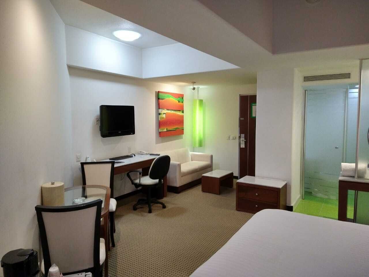 Habitación de hotel con cama, escritorio, silla, televisor y ducha de vidrio.