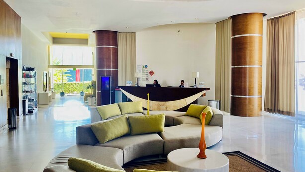 Un moderno vestíbulo de hotel con un mostrador de recepción curvo, un sofá modular y una mesa de centro redonda.