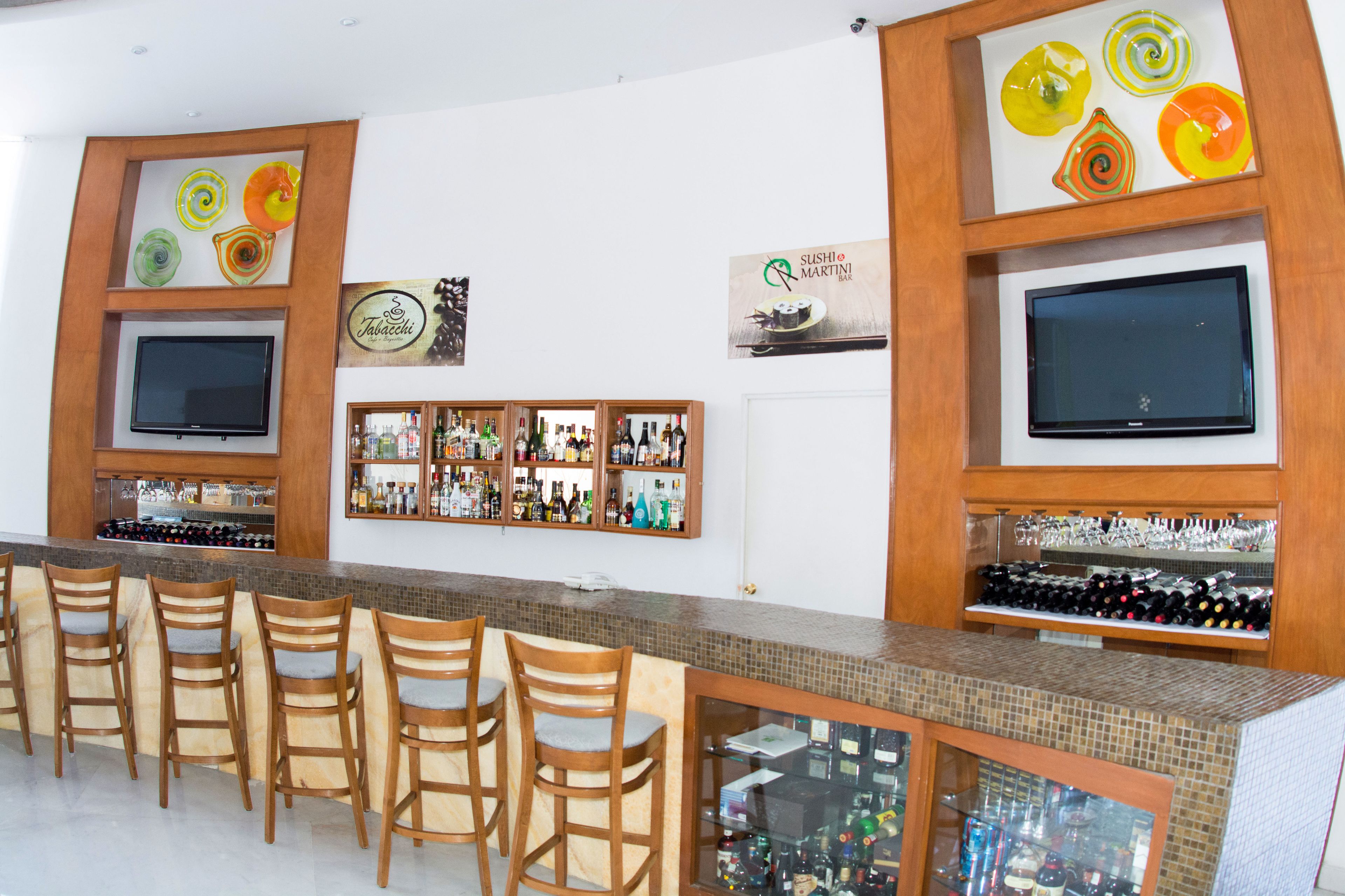A bar area with wooden chairs, a tiled counter, and shelves displaying bottles and glasses.