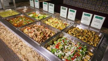 A buffet with various food options including meats, vegetables, and potatoes.