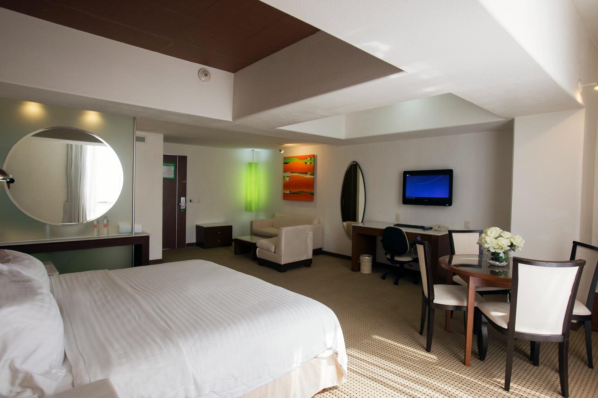 A hotel room with a large bed, a desk with a chair, a television, and a mirror.