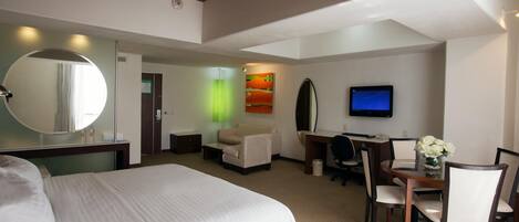 A hotel room with a large bed, a desk with a chair, a television, and a mirror.