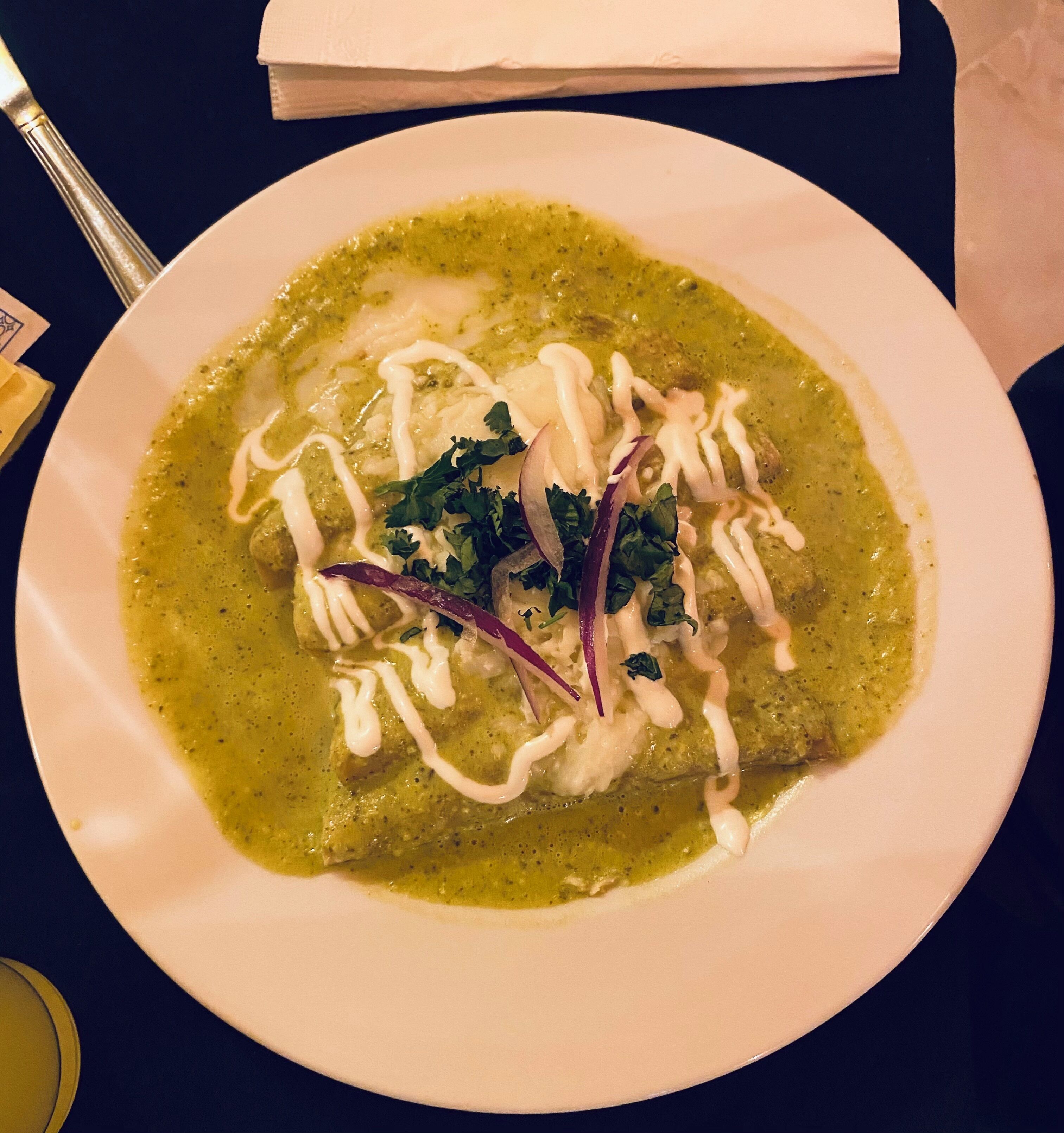 A plate of food with a green sauce, white cream, and red onion garnish on a white plate.