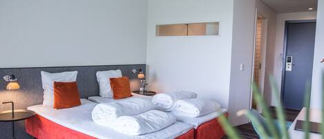 Une chambre d’hôtel avec un grand lit, deux tables de chevet avec des lampes, un mur d’accent rouge et une porte donnant sur une autre pièce.