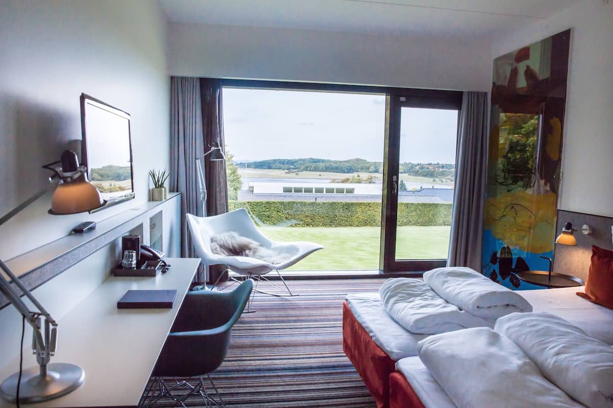 Hotellihuone, jossa on suuri ikkuna, työpöytä tuolilla, sänky ja taulu seinällä.