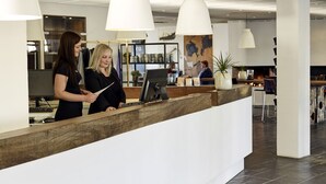 A reception area with a wooden counter, a computer, and a large map on the wall. - Comwell Roskilde (Roskilde)