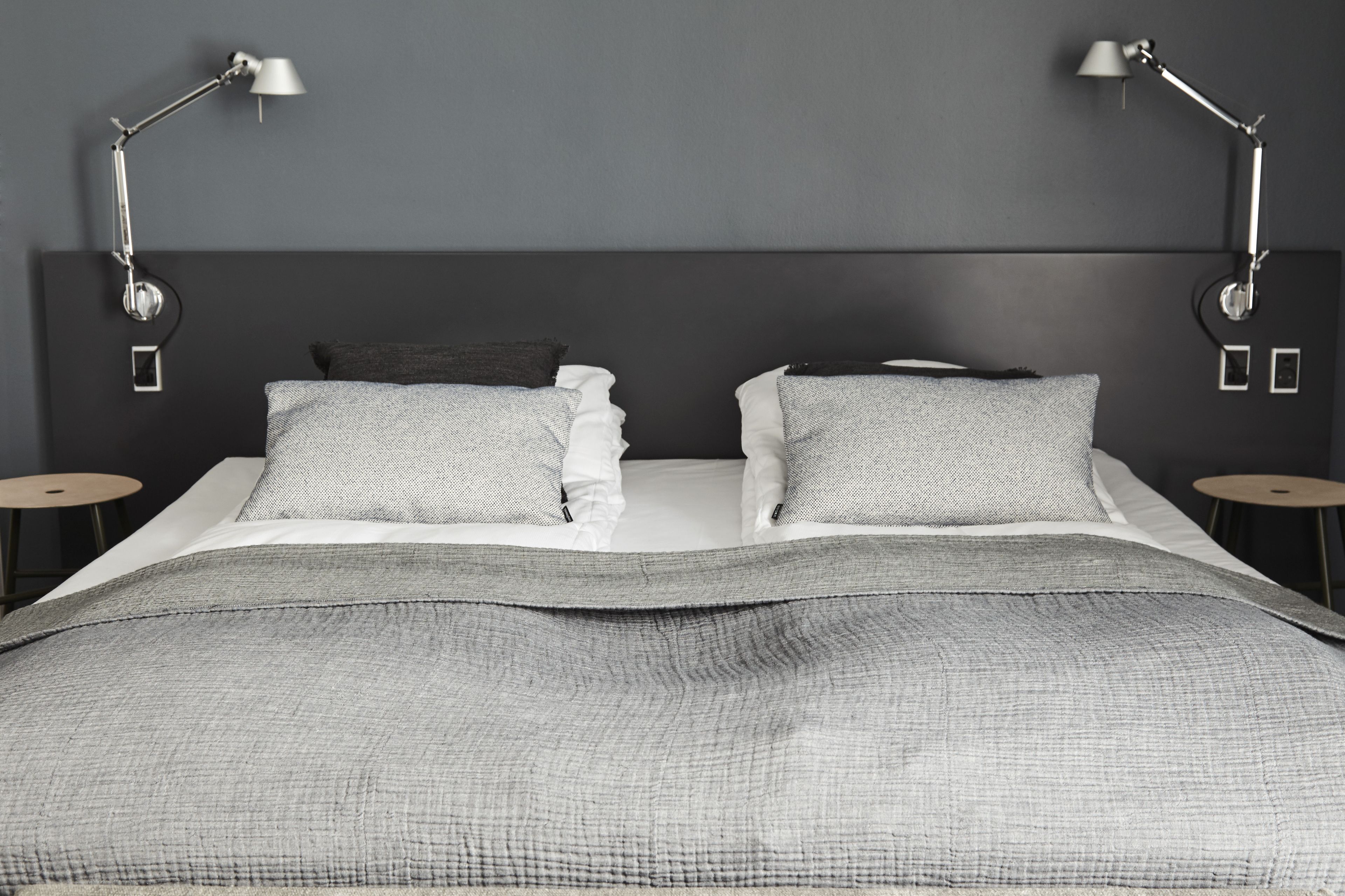 Une chambre à coucher moderne avec un grand lit, deux tables de chevet et deux lampes fixées au mur.