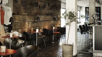 A modern interior with round tables and black chairs, a large wooden wall, and a potted plant.