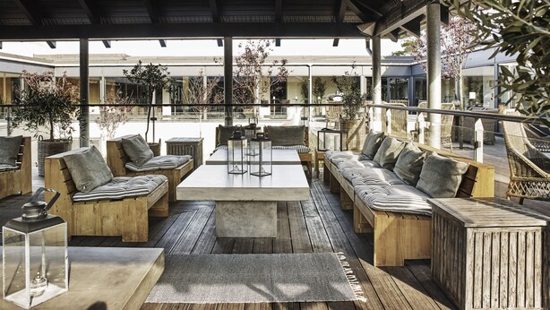 An outdoor seating area with wooden furniture, a concrete table, and hanging lanterns. - Comwell Roskilde (Roskilde)