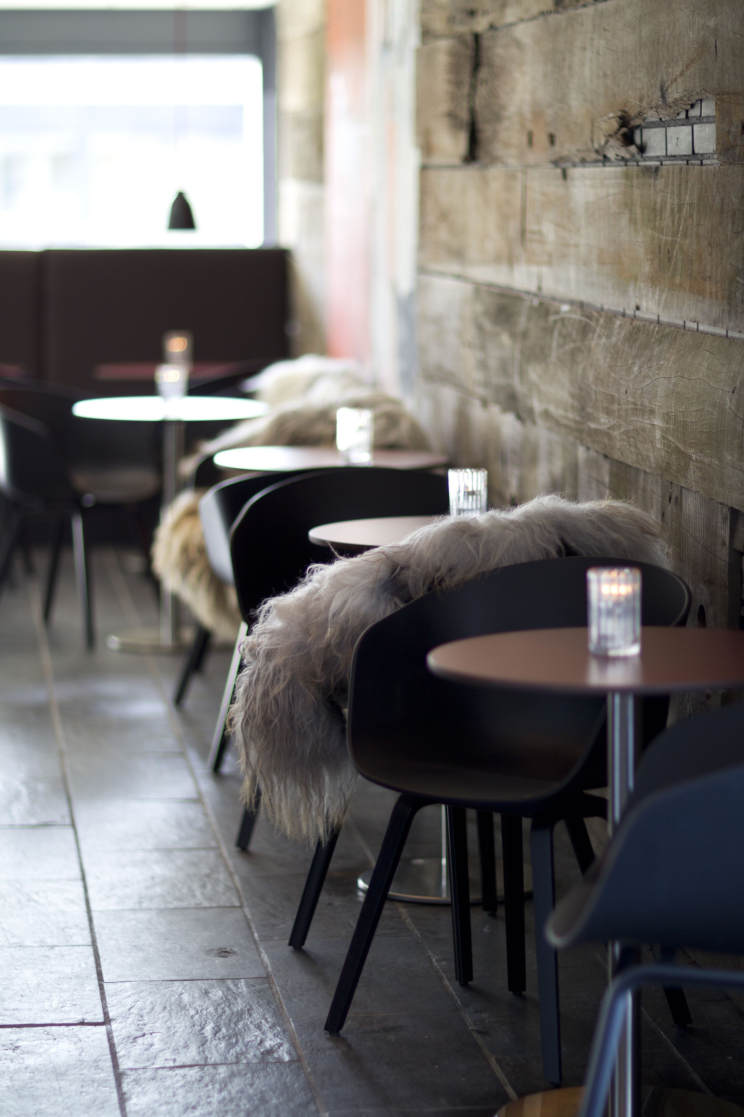 A row of tables with chairs, some with fur throws, in a cafe setting.