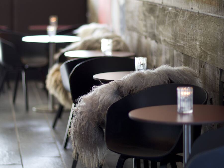 A row of tables with chairs, some with fur throws, in a cafe setting.