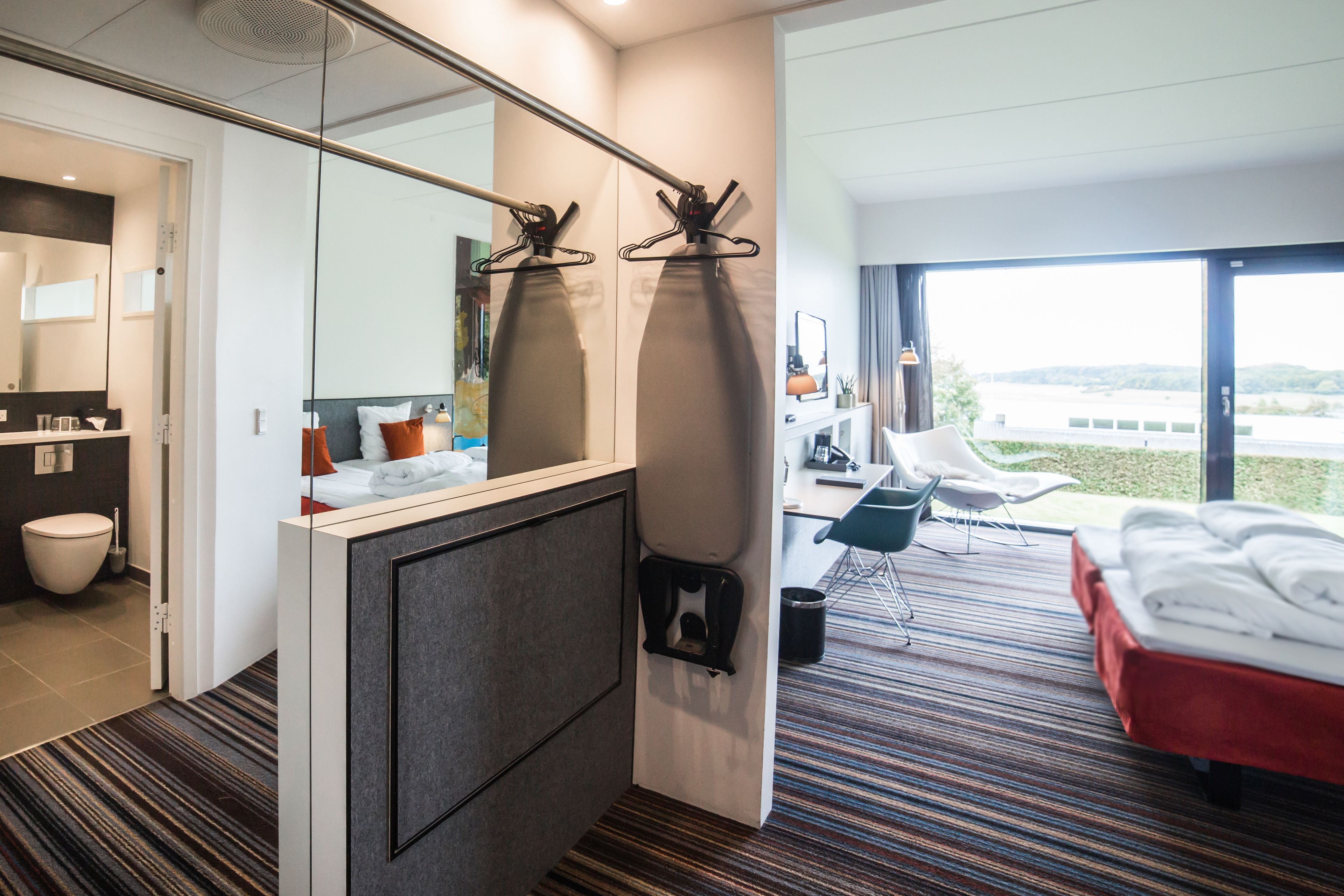 Quarto de hotel moderno com banheiro, cama, área de estar e vista para o exterior.