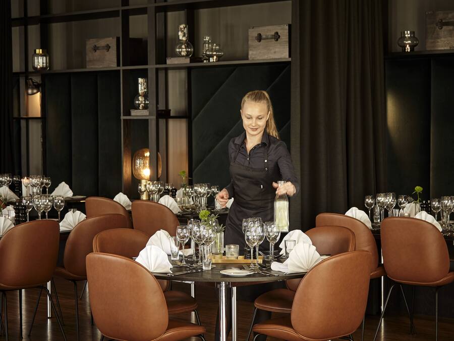 En restaurangmiljö med flera bord som är dukade för middag, och varje bord har stolar, glas och bestick.