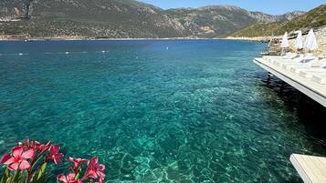 Une mer d’un bleu profond, avec un quai et des parasols blancs, le tout entouré de montagnes.
