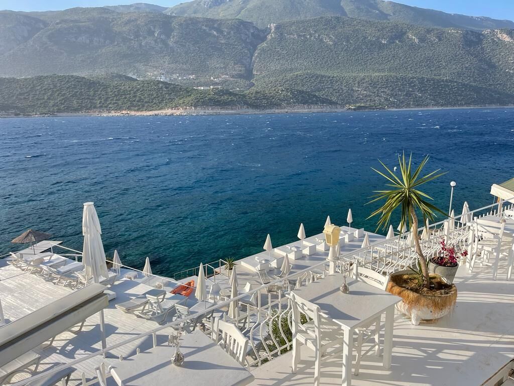 Une terrasse dotée de mobilier blanc et offrant une vue sur la mer et les montagnes.