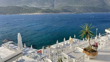 Une terrasse dotée de mobilier blanc et offrant une vue sur la mer et les montagnes.