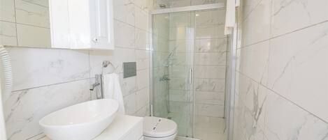 A bathroom with a white sink, toilet, and glass-enclosed shower.