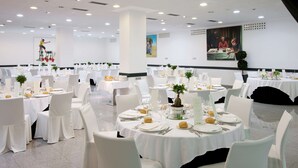 A banquet hall with round tables set for dining, white chairs, and a modern ceiling with recessed lighting.